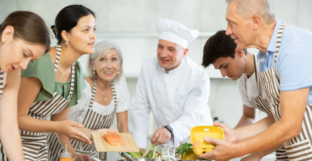 Vue en plongée de plusieurs mains de participants travaillant simultanément sur une pâte et des éléments de pâtisserie sur un plan de travail en marbre lors d'un atelier professionnel
